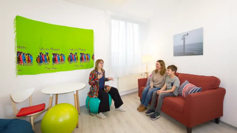 Psychotherapie für Kinder und Jugendliche - Mutter und Sohn auf roter Couch mit Therapeutin